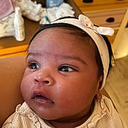 Aïana a rejoint le concours — aidez-le/la à gagner de superbes lots ! baby, infant, headband, clothing, face, eyes, curious, portrait, indoor, ruffled_top, wooden_drawers, baby_supplies, skin, cute, child, person, closeup, soft_lighting, head, young
