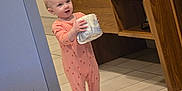 Keira is registered to the contest to win money with this photo: baby, bathroom, cabinetry, child, clothing, curious, floor_tiles, holding, home, indoor, light, person, pink_onesie, standing, tile_floor, toddler, toilet_paper, towels, wooden_cabinet, young_child