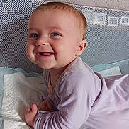 Aliyah is registered to the contest to win money with this photo: baby, infant, smile, happy, tummy, onesie, purple_clothing, face, child, cute, indoors, resting, young_child, skin, head, hands, blue_eyes, short_hair, fabric, background