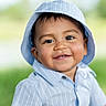 child, toddler, portrait, smiling, happy, outdoor, sun_hat, striped_shirt, blue_clothing, short_sleeves, face, eyes, teeth, cheeks, brown_hair, greenery, blurred_background, daylight, closeup, photography