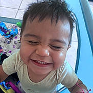 Dylan joined the competition — help win amazing prizes! child, toddler, baby, smiling, happy, portrait, face, close_up, indoors, playroom, toys, colorful, yellow_shirt, short_hair, eyes_closed, teeth, joyful, playful, bracelet, photography