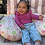 baby, smiling, child, curly_hair, pink_shirt, blue_pants, socks, pillow, owl_pattern, cushion, chair, outdoor, sunlight, happy, portrait, cute, infant, toddler, relaxed, fun