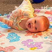 Jensen is registered to the contest to win money with this photo: baby, smiling, blanket, colorful, cartoon, blue_balloon, carpet, indoor, happy, infant, toddler, playtime, cute, child, face, clothing, lying_down, soft_toys, home, fun