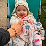 Jensen is registered to the contest to win money with this photo: baby, child, stroller, blanket, knitted_hoodie, bear_ears, smiling, blue_eyes, hand_holding, outdoor, grass, pavement, cute, happy, person, infant, clothing, warm, cozy, portrait