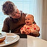 Jensen is registered to the contest to win money with this photo: baby, person, smile, happy, indoor, dining_table, plate, food, window, curtains, blinds, sweater, heart_pattern, table, adult, child, joy, family, casual_clothing, portrait