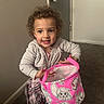 Katalaya is registered to the contest to win money with this photo: toddler, child, curly_hair, pink_bag, cartoon, indoor, carpet, hoodie, plaid_skirt, smiling, happy, person, young_child, playful, cute, holding, clothing, room, door, floor