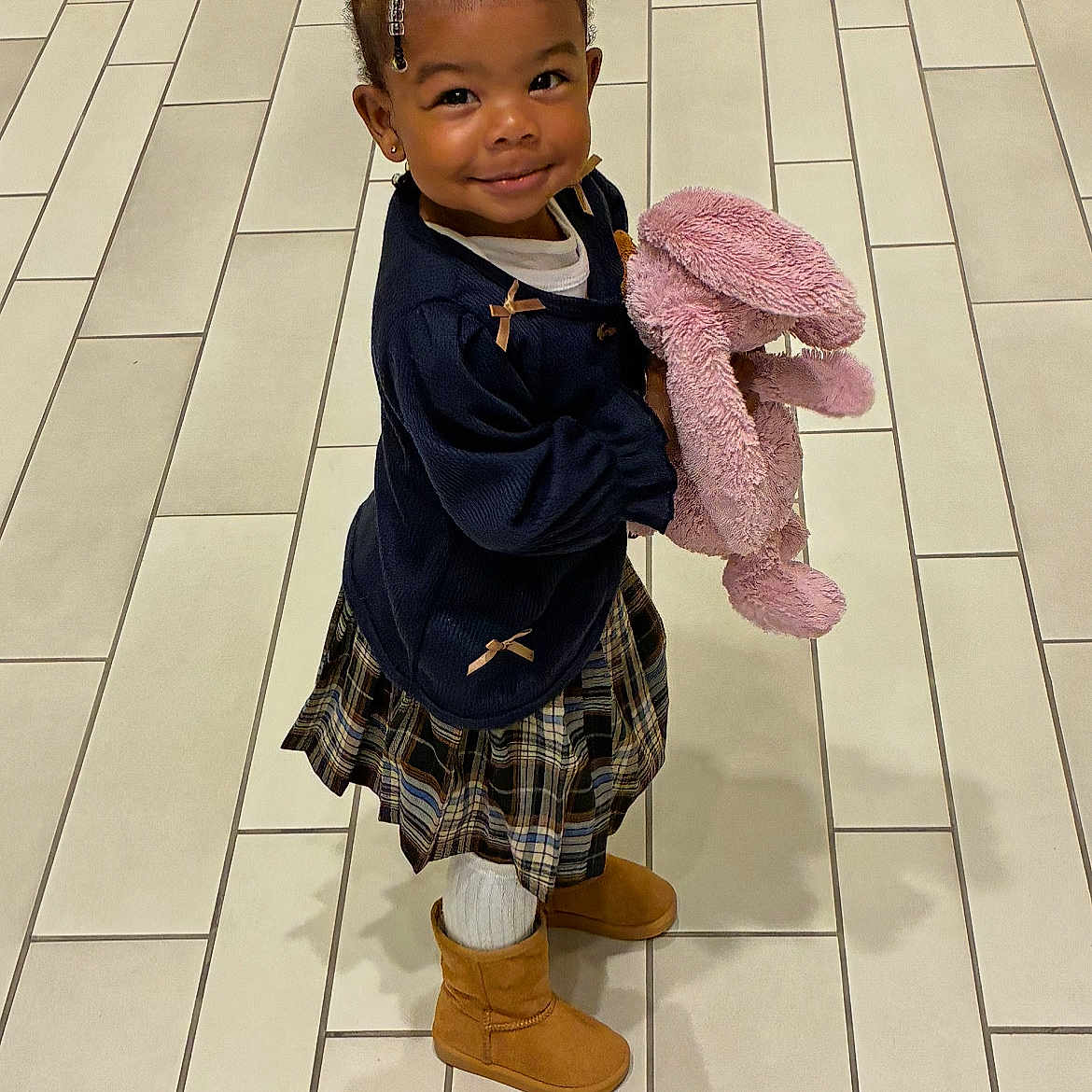 Jayonnē is registered to the contest to win money with this photo: accessories, braided_hair, child, cute, fashion, happy, indoor, navy_sweater, person, pink_bunny, plaid_skirt, portrait, smiling, standing, stuffed_animal, tan_boots, tile_floor, toddler, white_tights, young_child