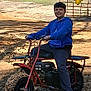 child, boy, smile, minibike, dirt_bike, outdoor, forest, trees, dirt, flag, blue_hoodie, casual_clothing, tire, vehicle, portrait, sunlight, sand, woodland, youth, recreation