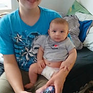 Tristen is registered to the contest to win money with this photo: child, baby, sibling, infant, video_game_controller, controller, tshirt, diaper, bed, pillow, blanket, indoor, portrait, smile, motion_blur, sitting, hands, casual_clothing, floor, room