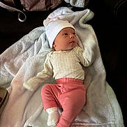 Oakleigh joined the competition — help win amazing prizes! baby, infant, hat, pink_pants, white_socks, cream_sweater, blanket, soft_texture, brown_bag, lying_down, curious_expression, indoor, cozy, cute, child, person, headwear, fabric, resting, comfortable