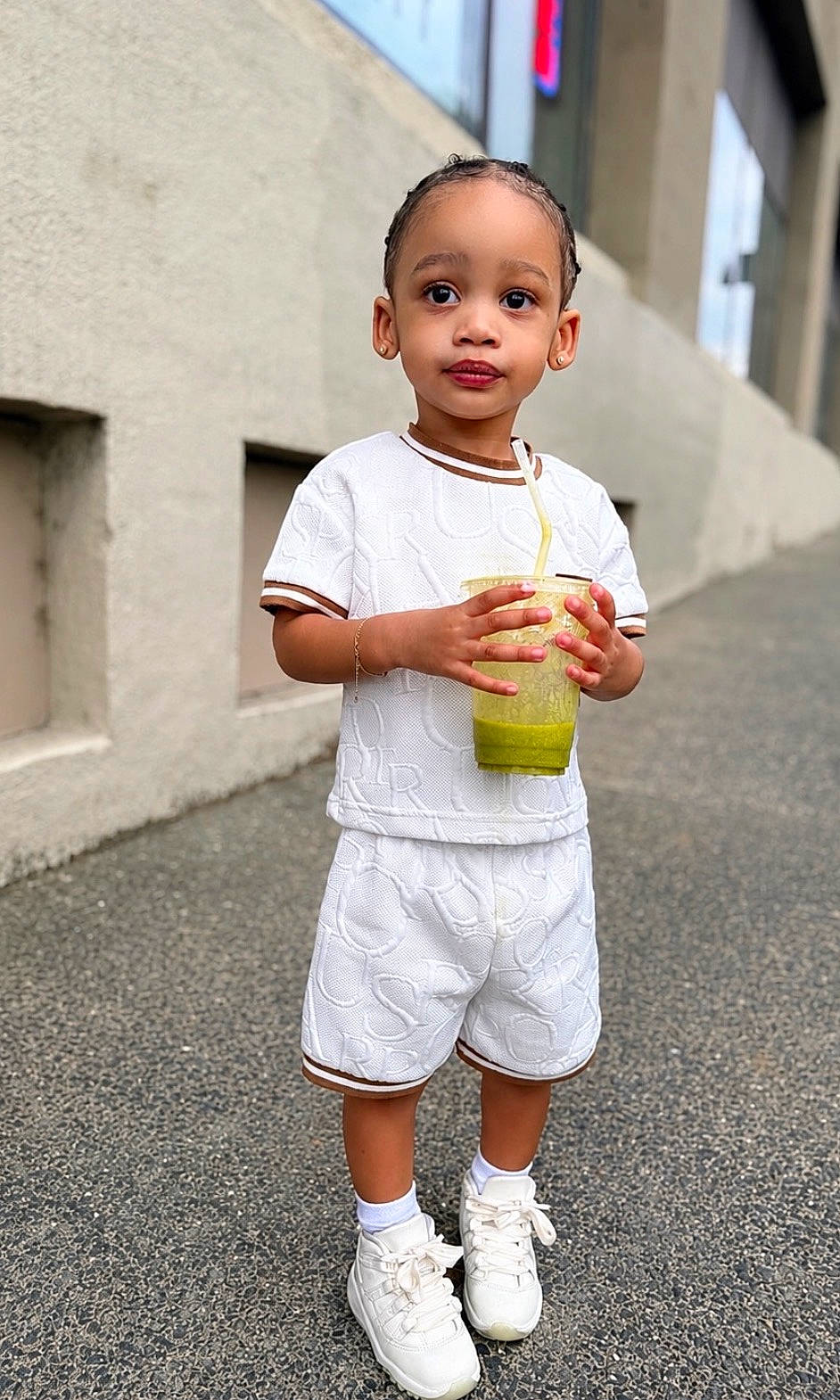 Chosyn joined the competition — help win amazing prizes! architecture, braided_hair, building, child, cup, daylight, drink, earrings, fashion, full_body, outdoor, pavement, portrait, shorts, smiling, sneakers, standing, straw, toddler, white_outfit