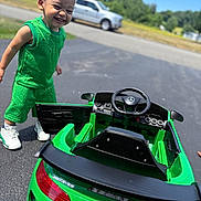 Chosyn joined the competition — help win amazing prizes! toddler, child, green_outfit, toy_car, mercedes, outdoor, smiling, happy, asphalt, sunny, daytime, vehicle, steering_wheel, play, transportation, casual_clothing, earrings, short_hair, small_car, background_blur