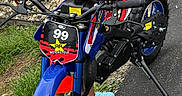 Chosyn joined the competition — help win amazing prizes! child, toddler, smiling, happy, outdoor, motorcycle, dirt_bike, toy_vehicle, rider, helmetless, braids, earrings, blue, red, pavement, grass, gravel, patio, chairs, portrait