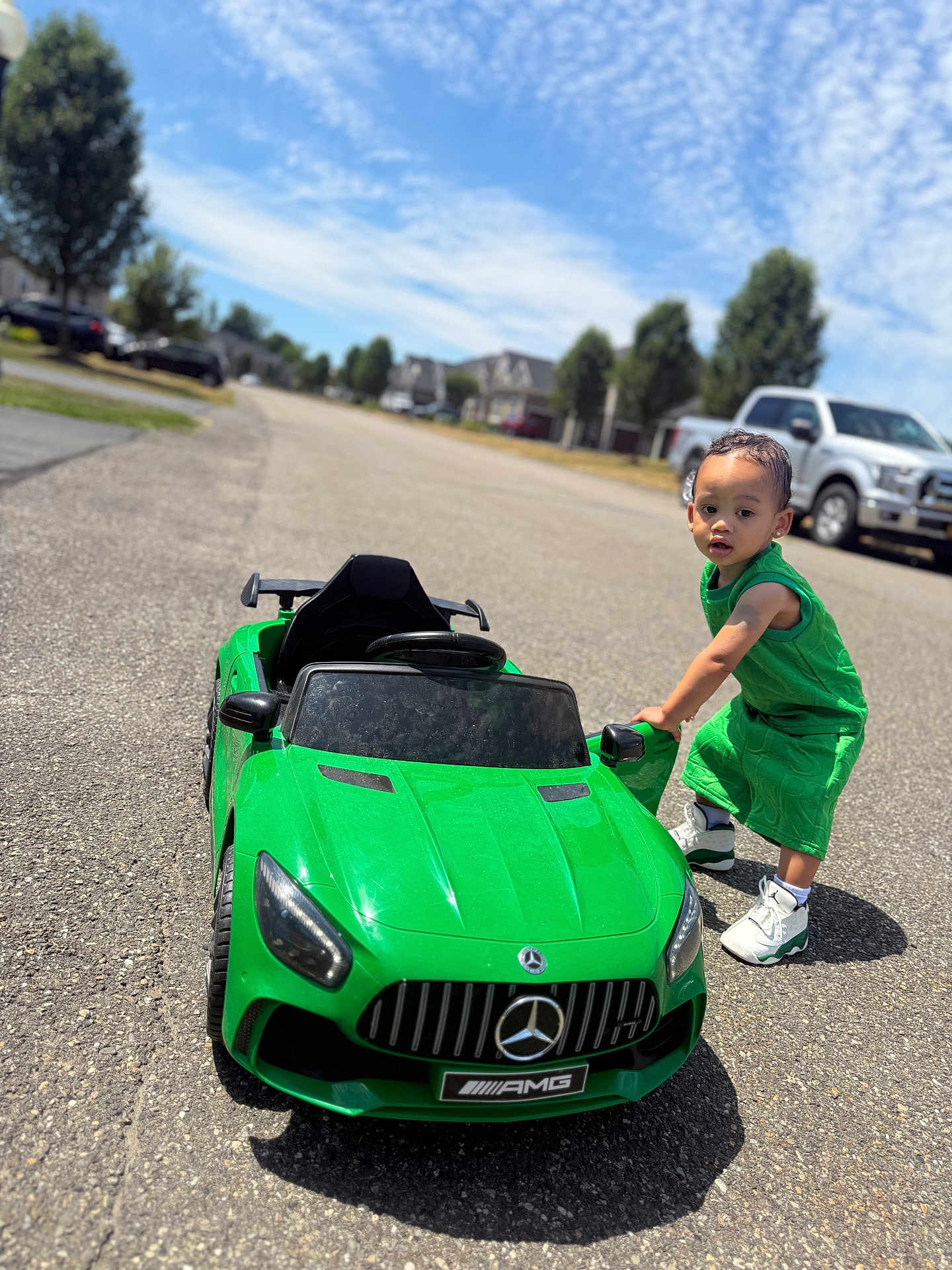 Chosyn joined the competition — help win amazing prizes! child, toddler, toy_car, green_clothing, outdoor, street, sunny, sky, clouds, vehicle, sneakers, sidewalk, residential_area, daytime, tree, car, road, play, kid, summer
