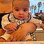 baby, child, person, arm, tattoo, hand, face, outdoor, restaurant, menu, table, umbrella, palm_tree, summer, clothing, bib, seat, adult, background, daylight
