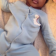 Pedro joined the competition — help win amazing prizes! baby, infant, onesie, blue_clothing, dinosaur_patch, bed, blanket, towel, lying_down, face, curious, indoors, soft_lighting, young_child, portrait, relaxed, child, sleepwear, person, cute
