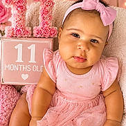 Nova is registered to the contest to win money with this photo: baby, infant, child, portrait, sitting, smiling, pink, dress, headband, bow, flowers, roses, birthday, eleven_months, sign, hearts, blanket, indoor, photography, celebration