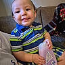 Caysen Journey joined the competition — help win amazing prizes! baby, child, toddler, smiling, tongue_out, sitting, couch, blanket, striped_clothing, plaid, bottle, pink_bottle, indoor, portrait, close_up, happy, face, hands, living_room, cozy