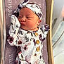 newborn, baby, infant, floral_outfit, headband, lying_down, bed, blanket, wooden_bed_frame, face, skin, clothing, button, purple, pattern, sleepwear, cute, portrait, indoors, person