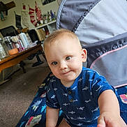 Finnigan is registered to the contest to win money with this photo: baby, blanket, blue_shirt, candid, carpet, child, curious, furniture, household_items, indoor, infant, living_room, person, playful, reaching_hand, seated, shark_pattern, smiling, stockings, table