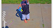 Zachary Brooks is registered to the contest to win money with this photo: toddler, child, barefoot, chalk, sidewalk, grass, tree, suburban, daylight, smiling, outdoor, person, street, shadow, clothing, tank_top, shorts, play, hand_gesture, summer
