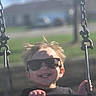 child, toddler, sunglasses, swing, outdoor, smile, happy, hair, playground, sunlight, daylight, fun, person, park, chain, seat, casual_clothing, joy, motion, recreation