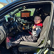 Jaxson joined the competition — help win amazing prizes! child, car, vehicle, driver_seat, smiling, open_door, computer_screen, sunlight, outdoor, tree, blue_sky, clothing, shoe, seat, dashboard, technology, person, happy, casual, daytime
