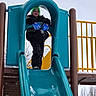 Jaxson is registered to the contest to win money with this photo: child, slide, playground, winter_clothing, gloves, hat, snow, outdoor, play, fun, smile, teal_slide, yellow_railings, park, cold_weather, happy, person, recreation, daytime, nature