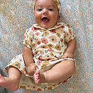 Jude is registered to the contest to win money with this photo: baby, smiling, floral_outfit, headband, barefoot, patterned_blanket, happy, infant, cute, child, portrait, lying_down, kicking, indoors, soft_lighting, cheerful, closeup, skin, person, joy