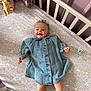 baby, denim_dress, crib, floral_sheet, toy, pacifier, smile, happy, infant, sleeping_area, fabric, child, furniture, soft_toy, pink_blanket, cute, indoors, person, face, legs
