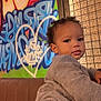 éden participe au concours pour gagner de l'argent avec cette photo : toddler, child, graffiti, heart, couch, sweater, jeans, urban, art, colorful, wall, portrait, indoor, curly_hair, casual_clothing, expression, person, young_child, background, relaxed
