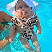 Amiyah is registered to the contest to win money with this photo: baby, child, pool, water, swimsuit, sunhat, leopard_print, playing, tongue_out, cute, smiling, summer, outdoor, person, hand, splash, fun, vacation, sunlight, happy