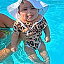 baby, child, pool, water, swimsuit, sunhat, leopard_print, playing, tongue_out, cute, smiling, summer, outdoor, person, hand, splash, fun, vacation, sunlight, happy