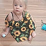 toddler, child, girl, sunflower_dress, indoor, wooden_floor, ball, sitting, blonde_hair, curly_hair, footwear, necklace, toy, chair, box, plastic_container, household_items, curious, casual, portrait