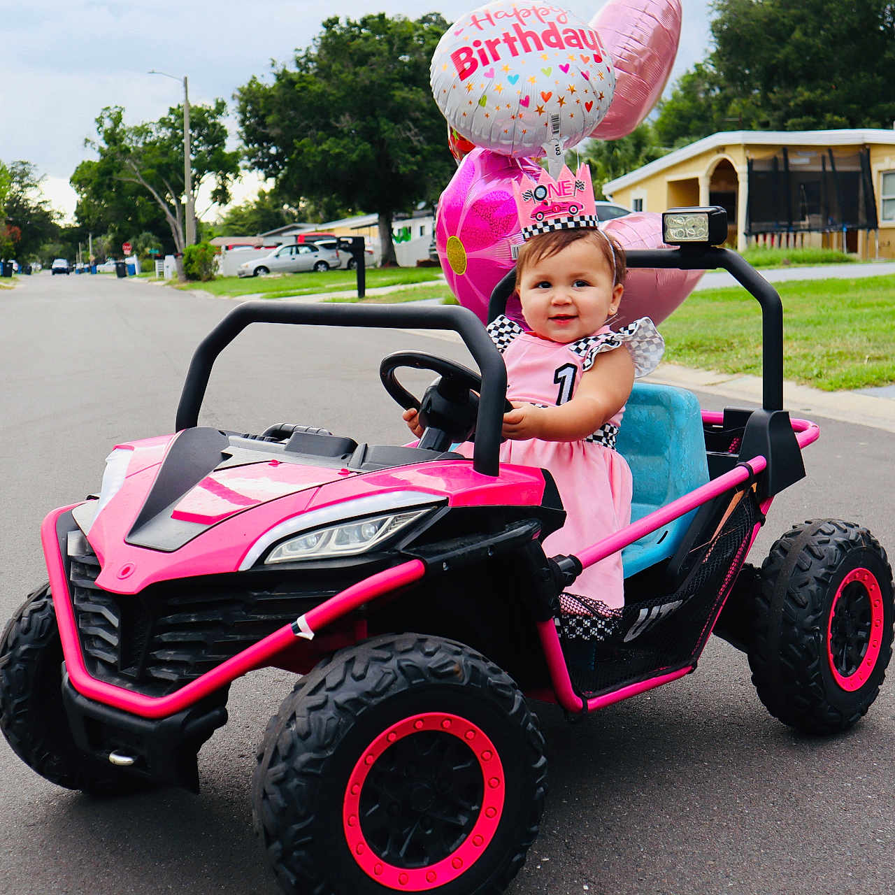 Alailah joined the competition — help win amazing prizes! toddler, birthday, toy_car, pink, balloons, dress, crown, smile, outdoor, street, suburban, child, celebration, happy, vehicle, one_year_old, daytime, grass, house, road