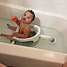 baby, bath_seat, bath_time, bathroom, bathtub, child, curly_hair, cute, expression, funny_face, indoor, infant, naked, orange_toy, person, playing, sitting, tiles, toy, water