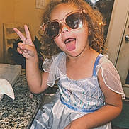 Eliza joined the competition — help win amazing prizes! casual, child, countertop, curly_hair, dress, girl, granite, home, indoor, kitchen, light, peace_sign, playful, princess_dress, seat, sign, smiling, sunglasses, tongue_out, wall_decor