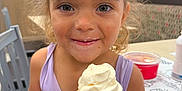 Eliza joined the competition — help win amazing prizes! child, ice_cream, cone, smile, curly_hair, indoor, table, chair, food, vanilla, happy, person, casual_dining, face, hand, purple_clothing, dessert, young, cute, fun