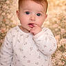 baby, infant, child, blue_eyes, onesie, flower_pattern, hand_on_mouth, portrait, soft_lighting, floral_background, cute, young, sitting, indoors, skin, face, head, expression, small_fingers, cozy