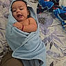 baby, infant, child, portrait, lying_down, swaddled, blanket, blue_blanket, bed, bedspread, floral_pattern, home, indoor, face, eyes_open, open_mouth, hand, adult_hand, cozy, colorful