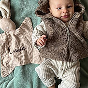 Lounis participe au concours pour gagner de l'argent avec cette photo : baby, infant, smiling, blanket, stuffed_toy, bunny, comforter, knitwear, vest, cozy, soft_texture, cute, child, portrait, laying_down, indoor, relaxed, person, warm_clothing, hand