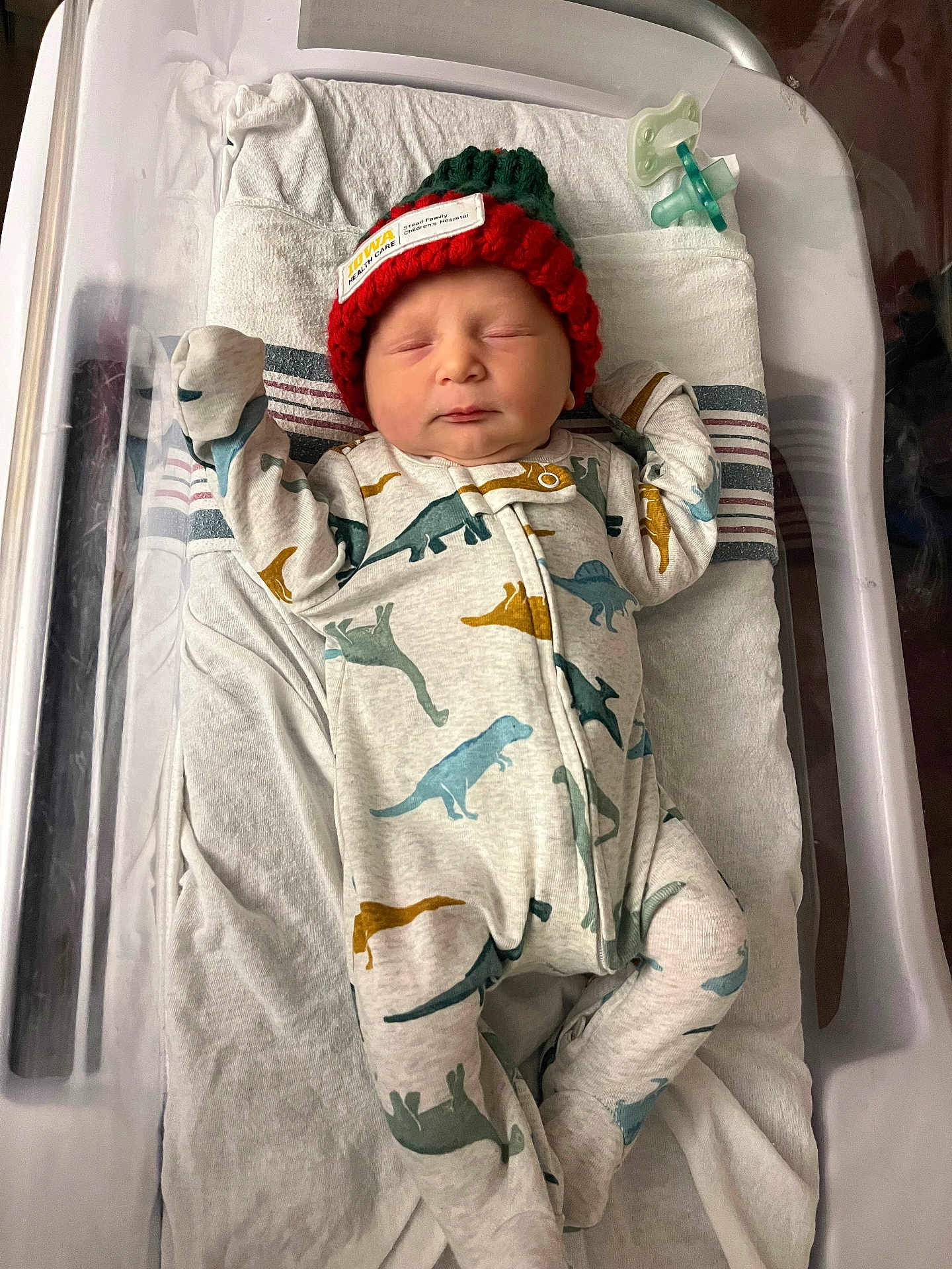 Axel joined the competition — help win amazing prizes! newborn, baby, infant, sleeping, onesie, dinosaur_pattern, hat, knit_hat, hospital, bassinet, pacifier, blanket, clothing, person, child, resting, cute, sleep, indoor, healthcare