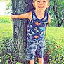 child, boy, barefoot, tree, grass, outdoor, smiling, tank_top, camouflage_shorts, nature, greenery, moss, playful, summer, dinosaur_print, happy, person, portrait, casual, daylight