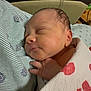 newborn, baby, sleeping, blanket, hand, face, infant, cozy, patterned_fabric, closeup, resting, peaceful, soft_lighting, indoor, cute, tiny, portrait, wrapped, bed, comfort