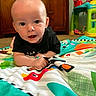 baby, child, infant, play_mat, colorful, indoor, toy, floor, carpet, toddler, face, eyes, mouth, clothing, black_shirt, wooden_furniture, background, curious, person, young