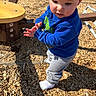 toddler, child, playground, wood_chips, blue_sweatshirt, grey_pants, socks, outdoor, daylight, sunlight, curious, exploring, young_child, person, clothing, playing, nature, fun, casual, active
