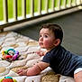 baby, child, infant, mattress, toy, colorful_toy, patterned_bedding, dark_shirt, crawling, indoors, railing, green_background, curious_expression, wide_eyes, soft_light, skin, hand, face, head, floor