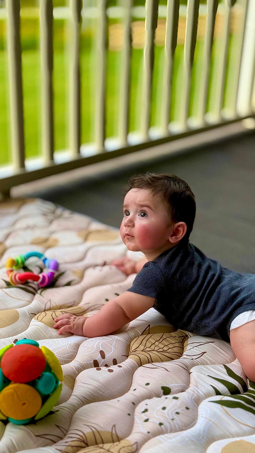 Grayson is registered to the contest to win money with this photo: baby, child, infant, mattress, toy, colorful_toy, patterned_bedding, dark_shirt, crawling, indoors, railing, green_background, curious_expression, wide_eyes, soft_light, skin, hand, face, head, floor
