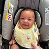 baby, bib, car_seat, child, closeup, clothing, colorful, cute, face, hand, happy, head, indoor, infant, person, safety_harness, seat_belt, sitting, skin, smile