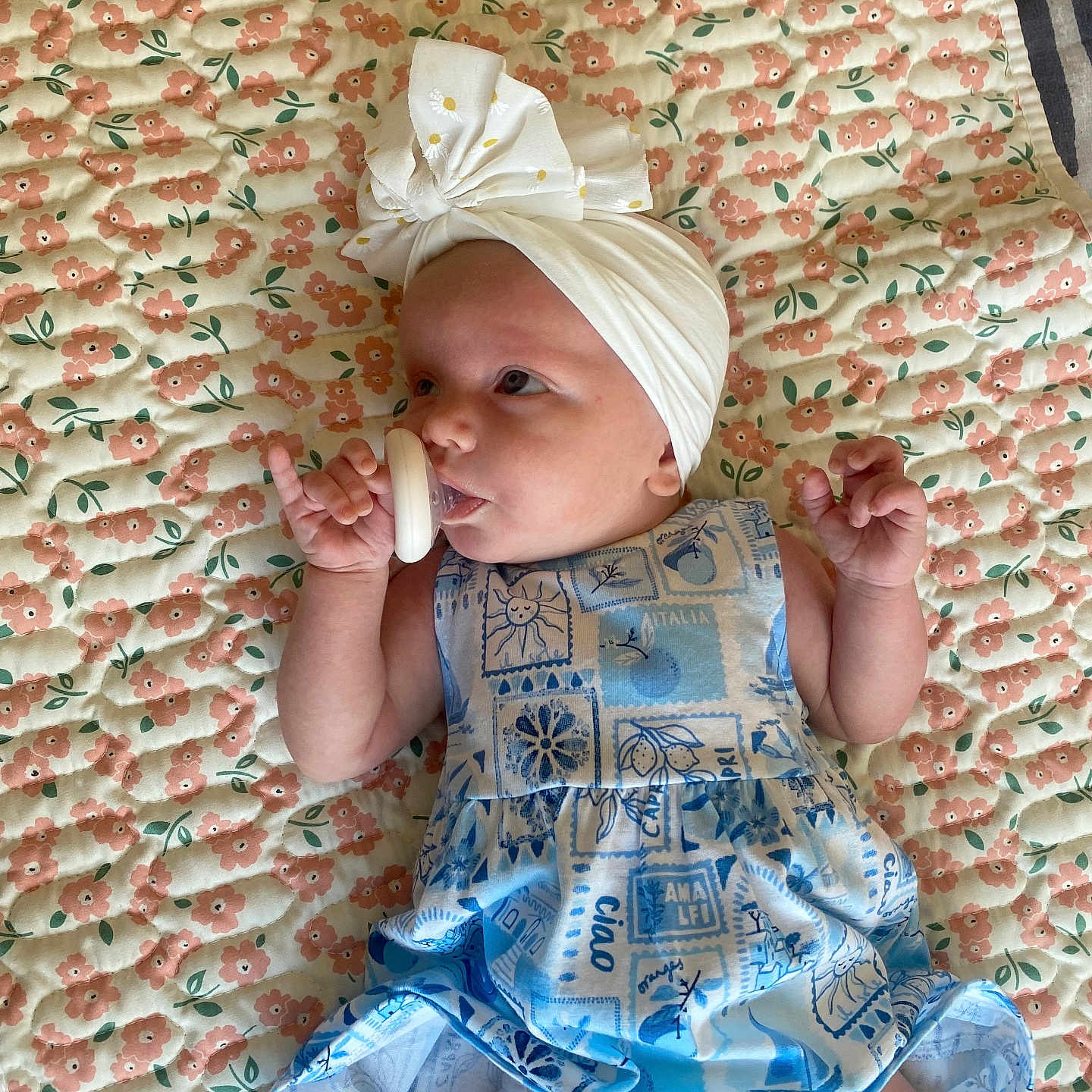 Poppy Rae is registered to the contest to win money with this photo: baby, blue_dress, bow, child, cute, diaper, dress, fabric, floral_quilt, headwrap, indoor, infant, lying_down, pacifier, patterned_clothing, pink_flowers, portrait, relaxed, small_hand, soft_lighting